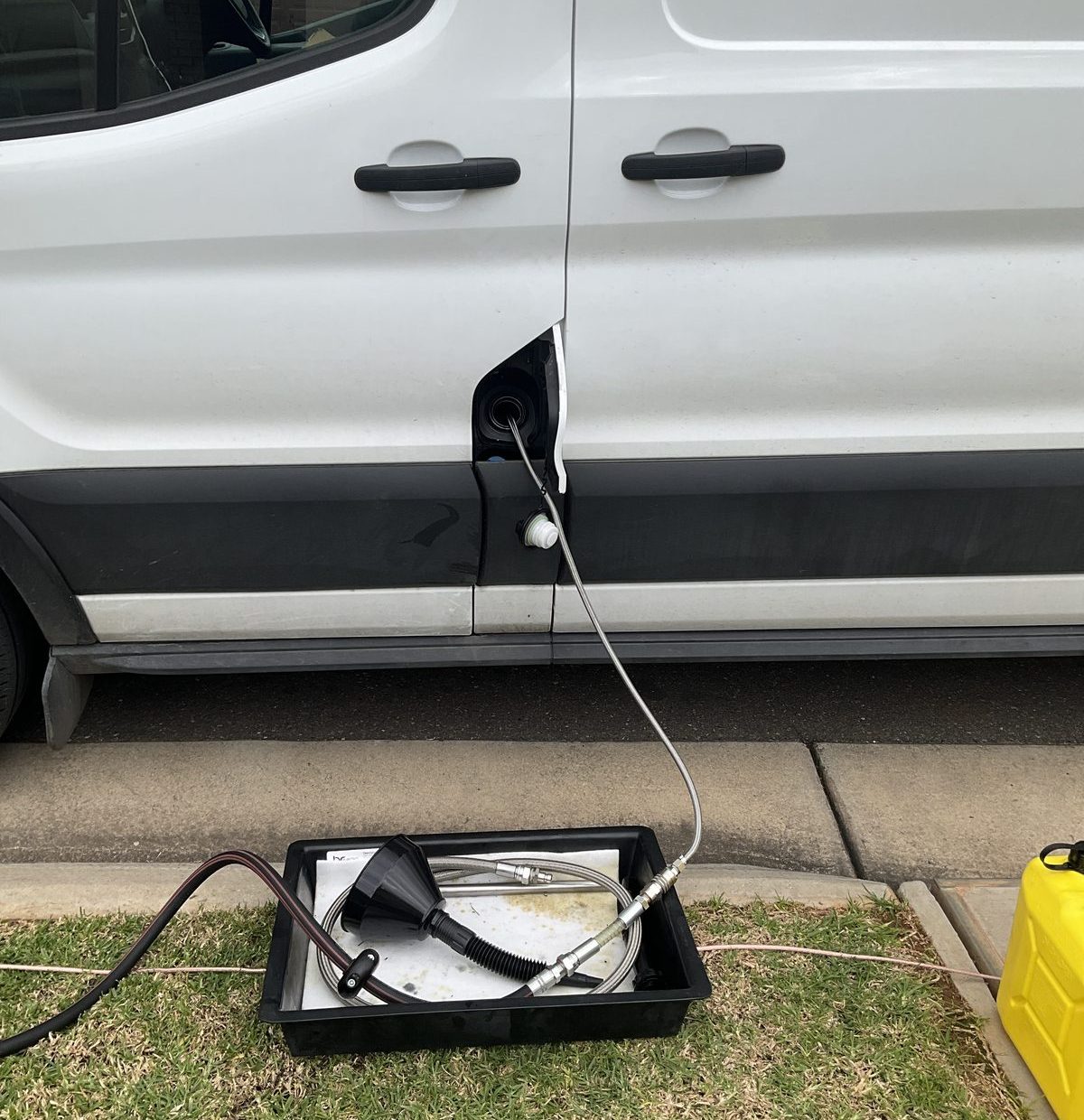 Drain hose in the filler neck of a white Ford Transit van at Parafield Gardens, spill tray and drum lines on the kerb