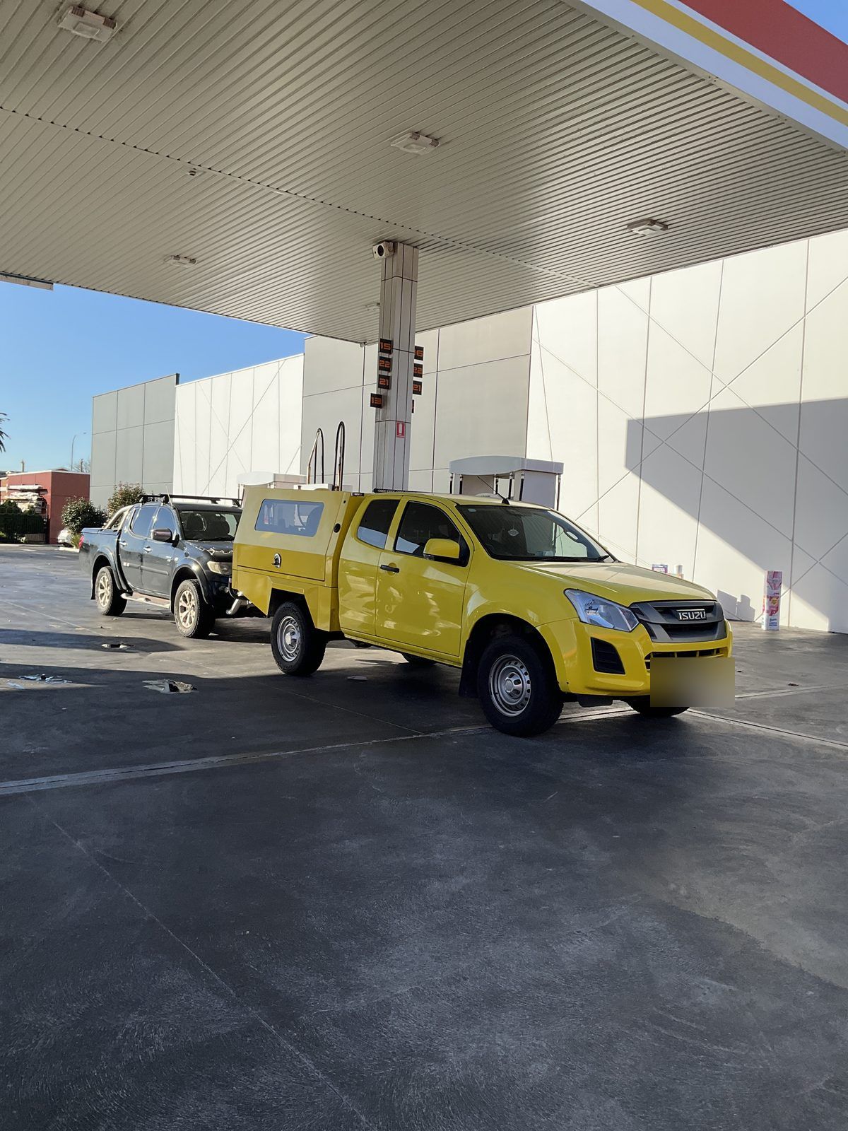 Grey Mitsubishi Triton and yellow service ute under a service station canopy, Port Adelaide