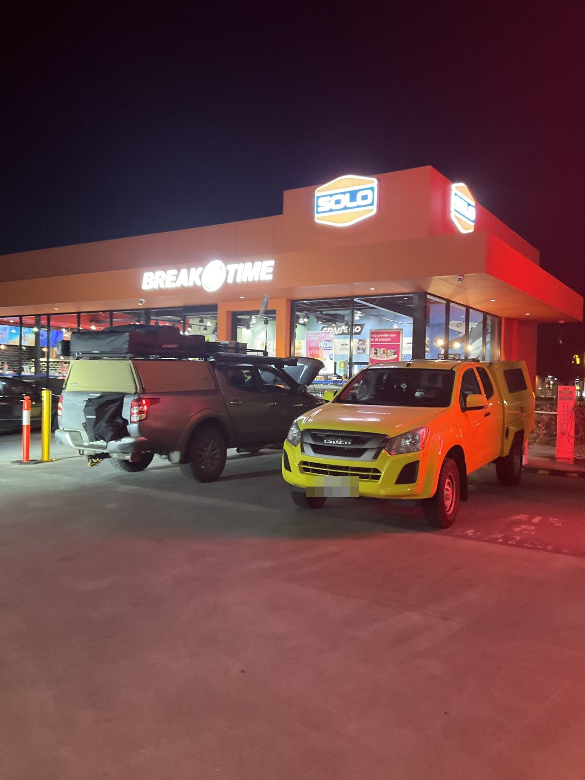 Dark dual cab ute and yellow service ute at a service station at night, Edinburgh North