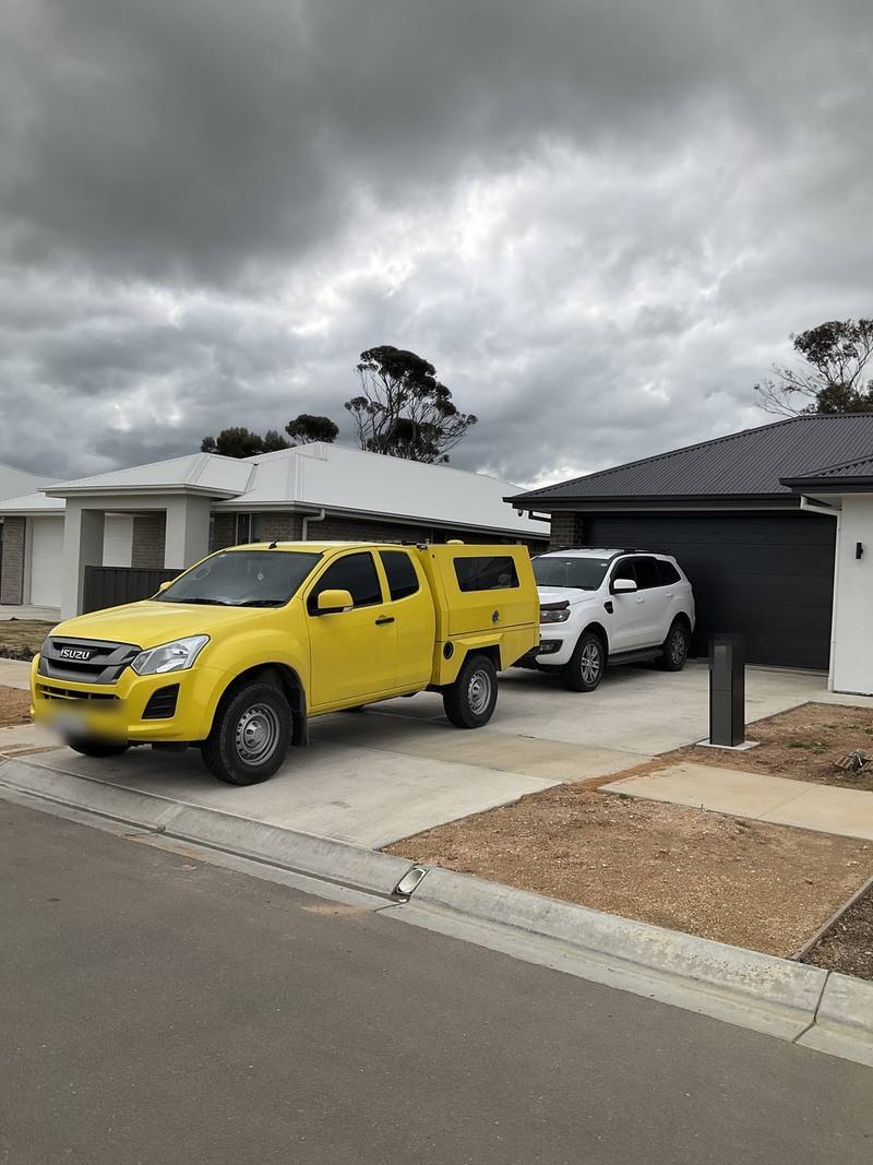 Yellow service ute and white Ford Everest parked in a driveway under a stormy sky, Murray Bridge