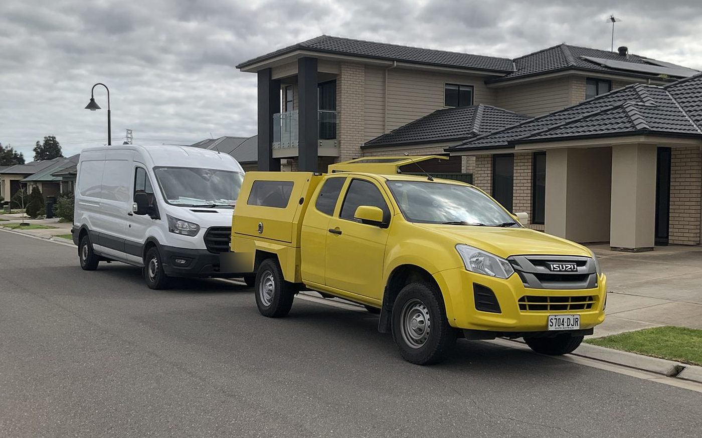 White Ford Transit van and yellow service ute parked on a suburban street, Parafield Gardens